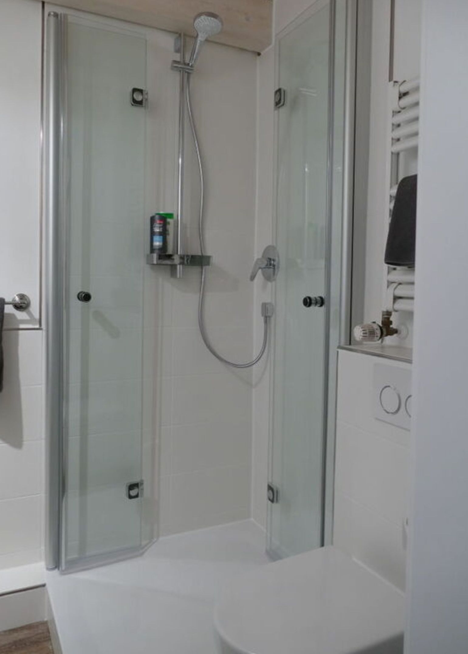 Una cabina doccia in vetro con soffione a mano e rubinetto a mano.