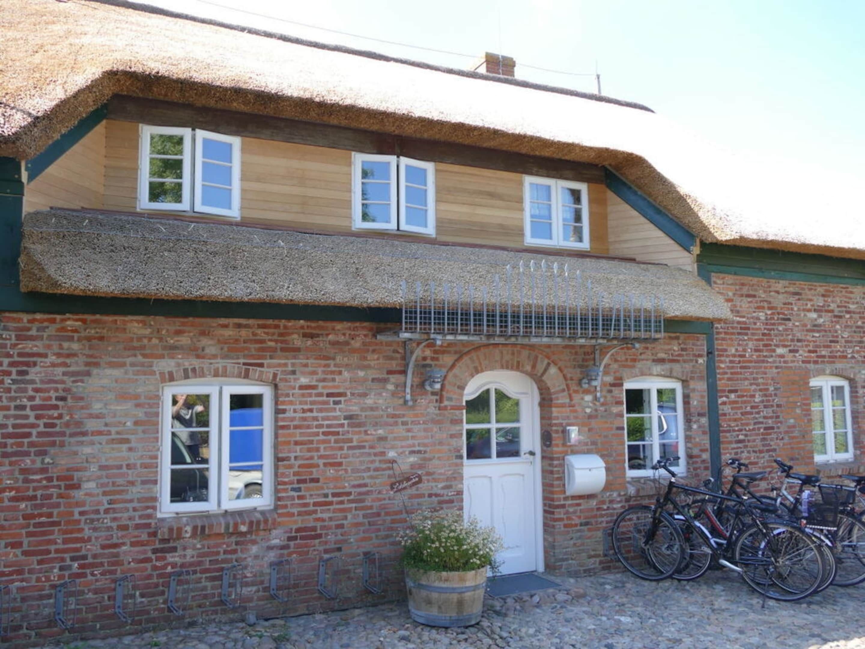 A traditional brick building with a thatched roof, a white door, and a small garden area with a potted plant.