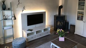 A modern living room with a flat-screen TV, a fireplace, a bookshelf, and a small table with a vase of flowers. - Favorite Place Modern Retreat (Wrixum)