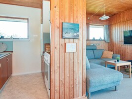 A cozy cabin interior with a kitchenette, a living area with a sofa and a television, and wooden walls.