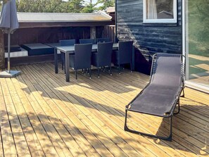 Une terrasse en bois avec une table et des chaises, un fauteuil de relaxation et un espace salon abrité.