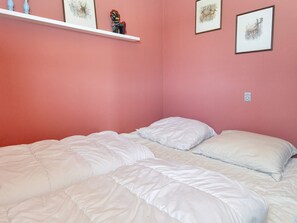 Une chambre avec deux lits, une étagère blanche ornée d’objets décoratifs et des œuvres d’art encadrées accrochées aux murs.