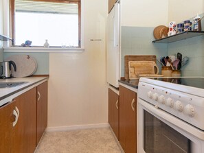 Une cuisine avec des meubles de rangement en bois, une cuisinière, une fenêtre et divers ustensiles de cuisine rangés sur les étagères.