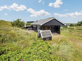 Una casa moderna con un garaje grande, rodeada de vegetación natural.