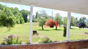 A covered porch with hanging flower baskets and a brick wall. - Mema and Pa’s Place (Byrdstown)
