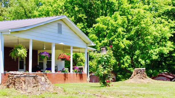 A white building with a porch, surrounded by greenery and trees. - Mema and Pa’s Place (Byrdstown)