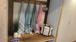 Ein Holzregal mit Handtüchern, einer Topfpflanze, einem Buch und einer Tasche mit der Aufschrift 'Beach Bum', in einem Hotelzimmer.
