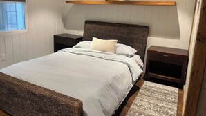 Ein Schlafzimmer mit Bett, Nachttischen, einem Holzregal und einem Fenster mit Jalousien.