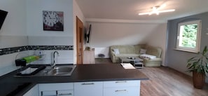Una cocina con lavamanos, encimera y armarios, un comedor con mesa y sillas, un sofá y una ventana con vistas.