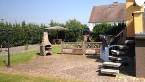 A backyard with a stone-built outdoor oven, a wooden deck, and a staircase leading to a house with a tiled roof. - Holiday Home \"baltic Sea Dream\" (Garz/Rügen)