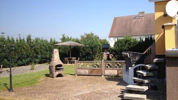 Um quintal com forno de pedra, um deck de madeira e uma escadaria que leva a uma casa com telhado em cerâmica.