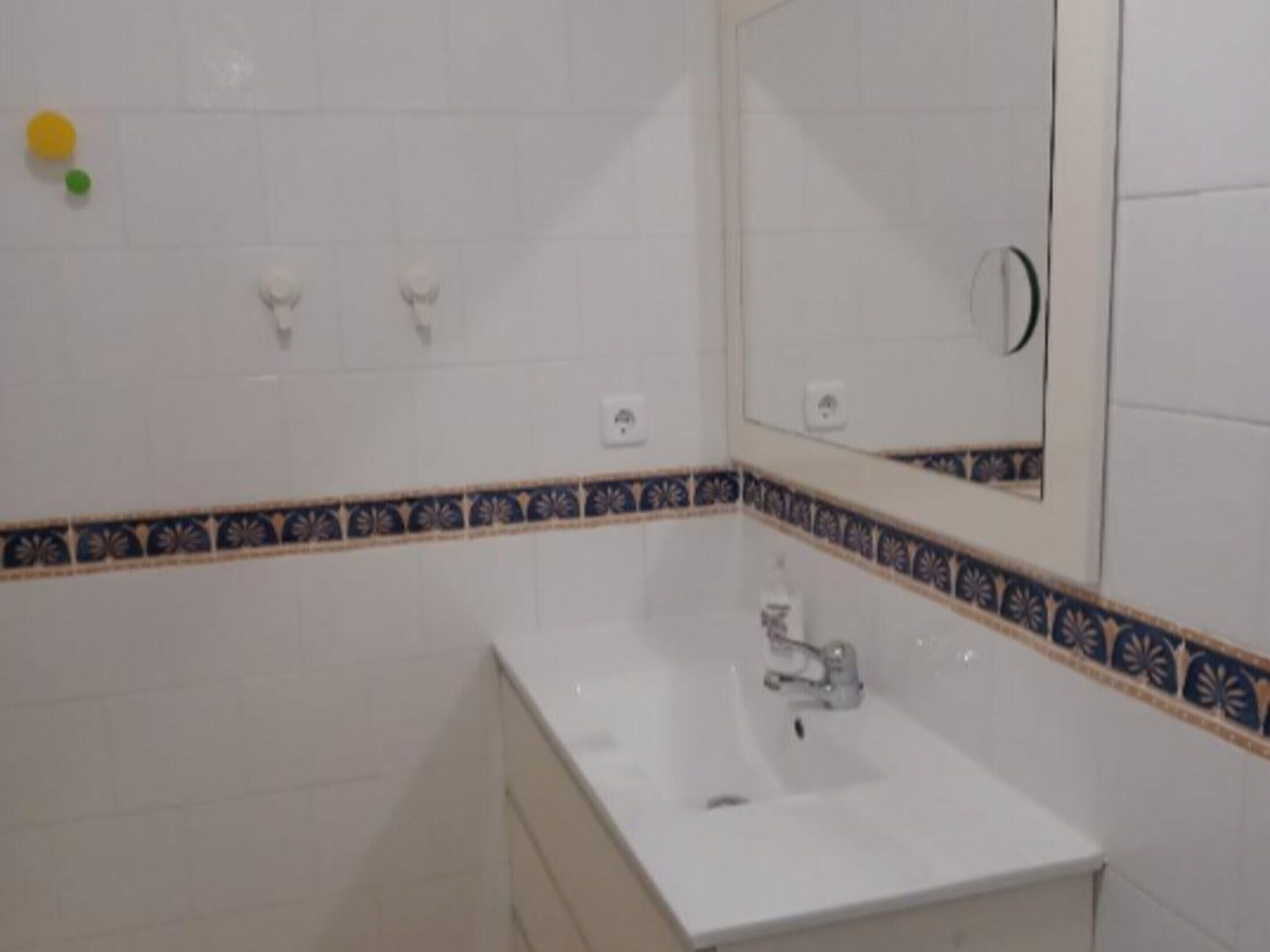 A bathroom with white tiles, a sink, a mirror, and a decorative border.