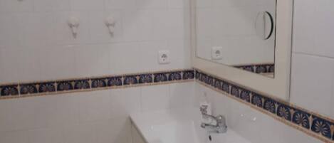 A bathroom with white tiles, a sink, a mirror, and a decorative border.