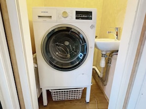 Een witte Siemens wasmachine in een kleine wasruimte, met een spoelbak en leidingen zichtbaar op de achtergrond.