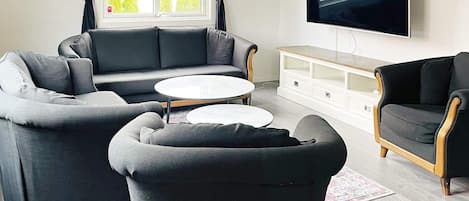 A modern living room with a sofa, armchairs, a coffee table, and a TV mounted on the wall.