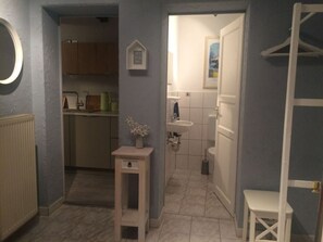 A compact kitchen with a small table and a vase of flowers, a white sink, and a toilet in a bathroom with a towel rack. - Guest House An der Truse (Brotterode-Trusetal)