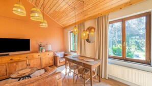 Ein modernes Wohnzimmer mit Holzboden, einem Essbereich und großen Fenstern mit Blick auf Grünflächen.
