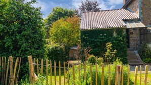 Ein Haus aus Stein mit einem Ziegeldach, umgeben von üppigem Grün und einem Holzzaun.