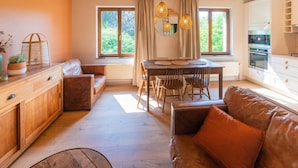 Ein gemütliches Wohnzimmer mit Holzbalkendecke, einer Essecke mit Tisch und Stühlen sowie einer Küche mit weißen Schränken.