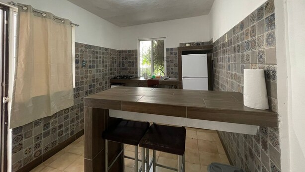 Une cuisine avec un mur recouvert de carreaux, un réfrigérateur, un évier et une fenêtre.