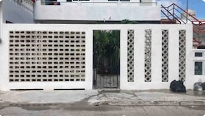 Un bâtiment blanc avec une entrée fermée par un portail, un portail en métal et une petite fenêtre.