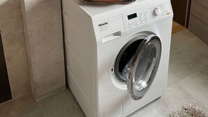 A compact, modern laundry room with a front-loading washing machine, a small shelf with decorative items, and a mirror above the machine. - Place to Be Modern Retreat (Georgenthal)