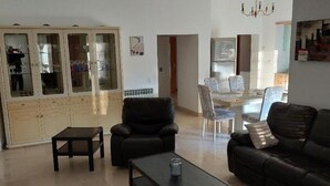 Una sala de estar con un sofá de cuero negro, una mesa de centro negra y un aparador con puertas de vidrio.