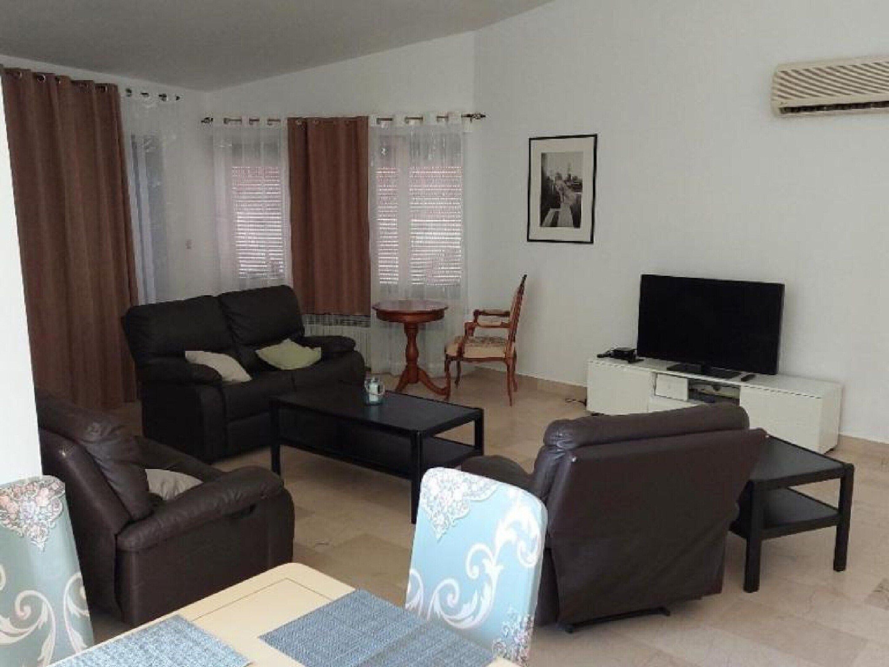 A living room with a sofa, chairs, a coffee table, a TV, and a small table.