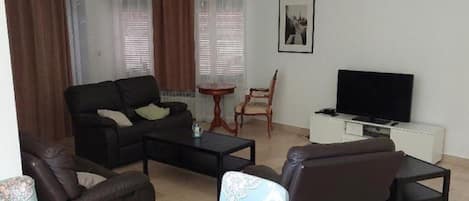 A living room with a sofa, chairs, a coffee table, a TV, and a small table.