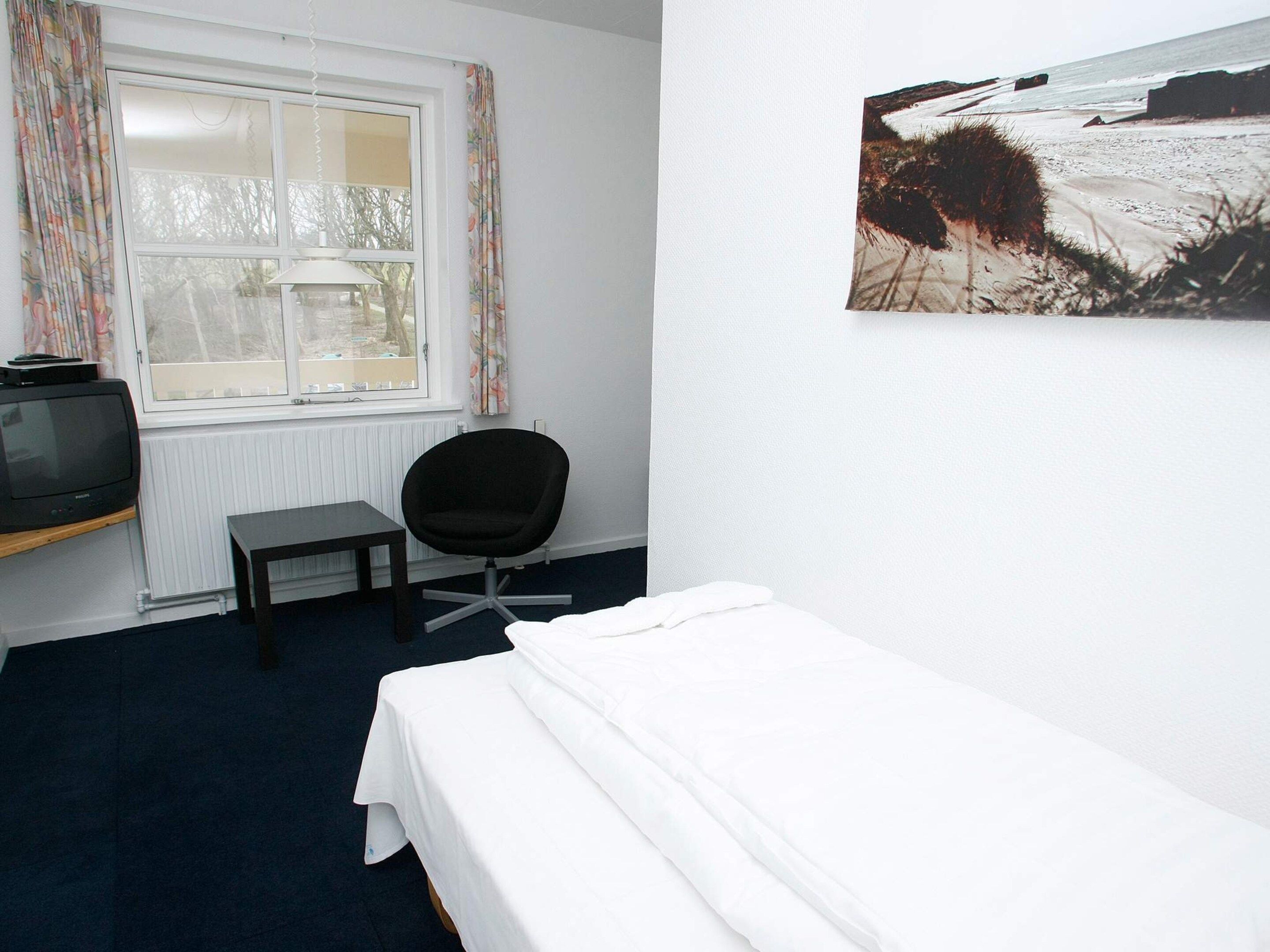 Une pièce comprenant un lit, une chaise, une table, un téléviseur et une fenêtre avec des rideaux.