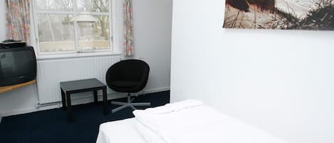 Une pièce comprenant un lit, une chaise, une table, un téléviseur et une fenêtre avec des rideaux.