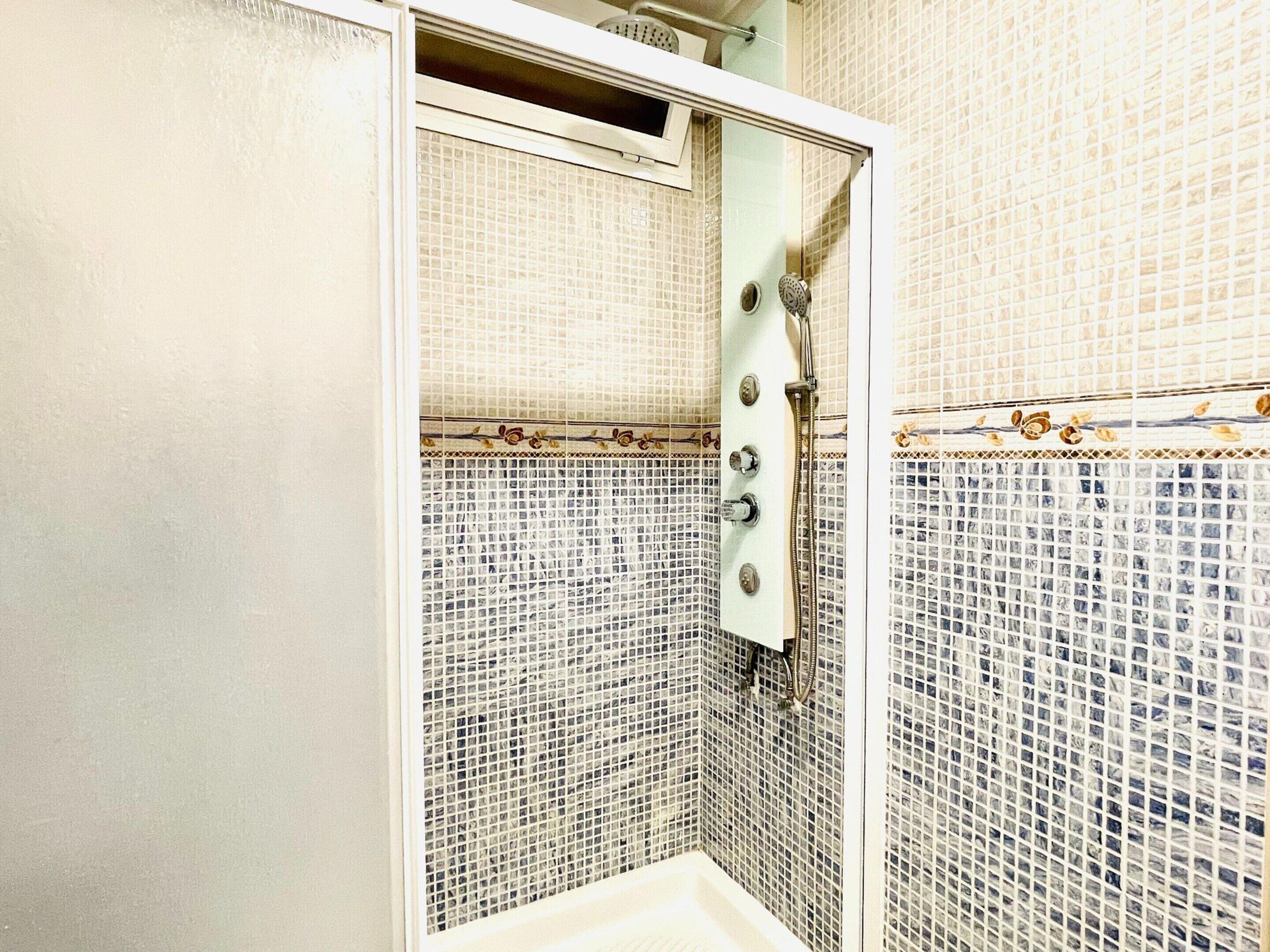 Een douche met een glazen deur, betegelde wanden en een douchekop.
