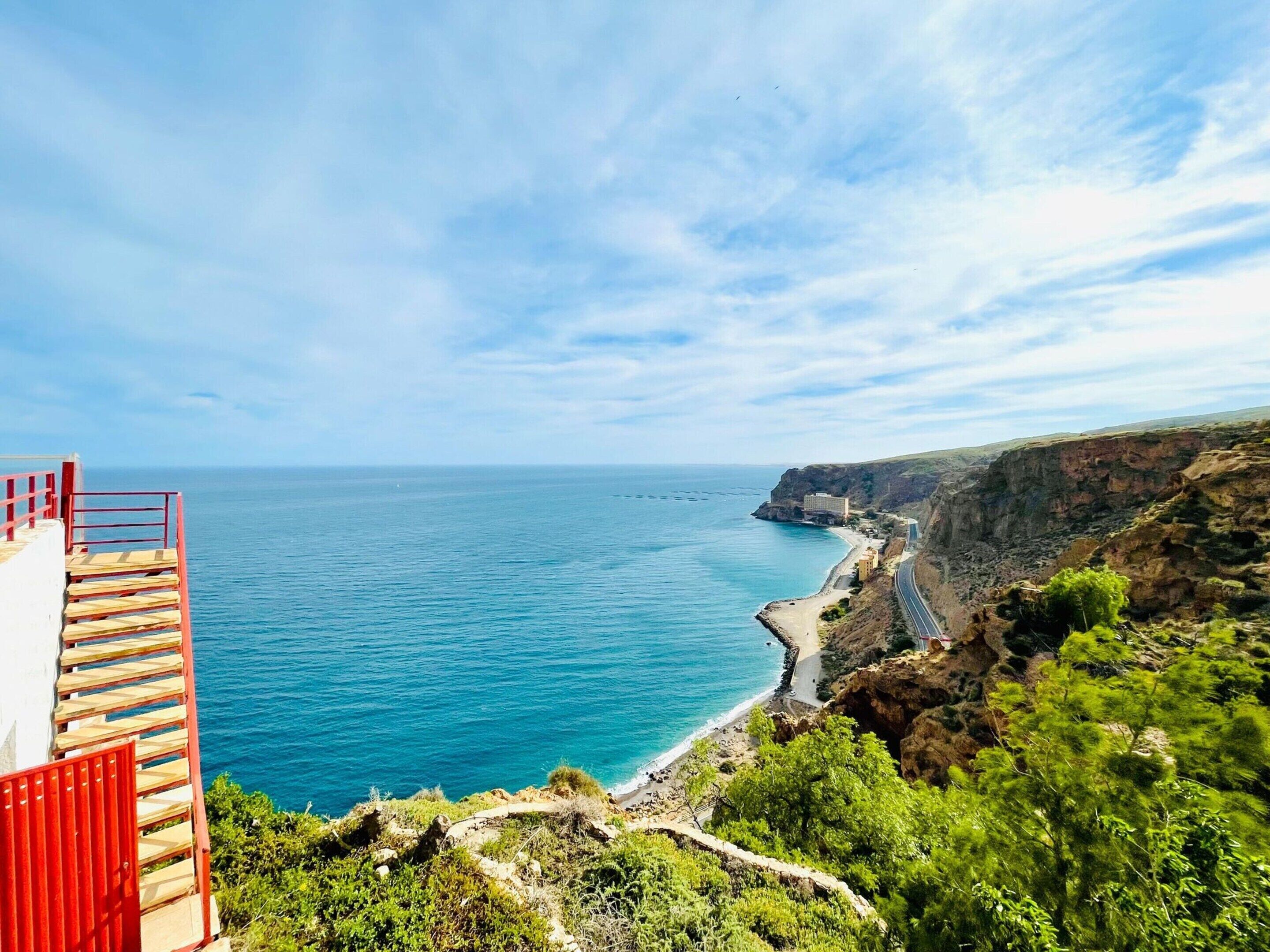 A coastal view with a clear sky, a beach, and a cliffside path.