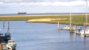 A marina with boats docked and a large ship in the distance. - Seehund Comfortable Holiday Residence (Otterndorf)