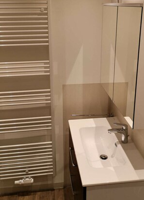 Une salle de bain moderne avec un lavabo blanc, un miroir et un porte-serviettes.