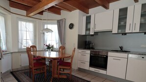 A kitchen with white cabinets, a stove, and a sink. There is a dining table with chairs and a rug. - Seehund Comfortable Holiday Residence (Otterndorf)