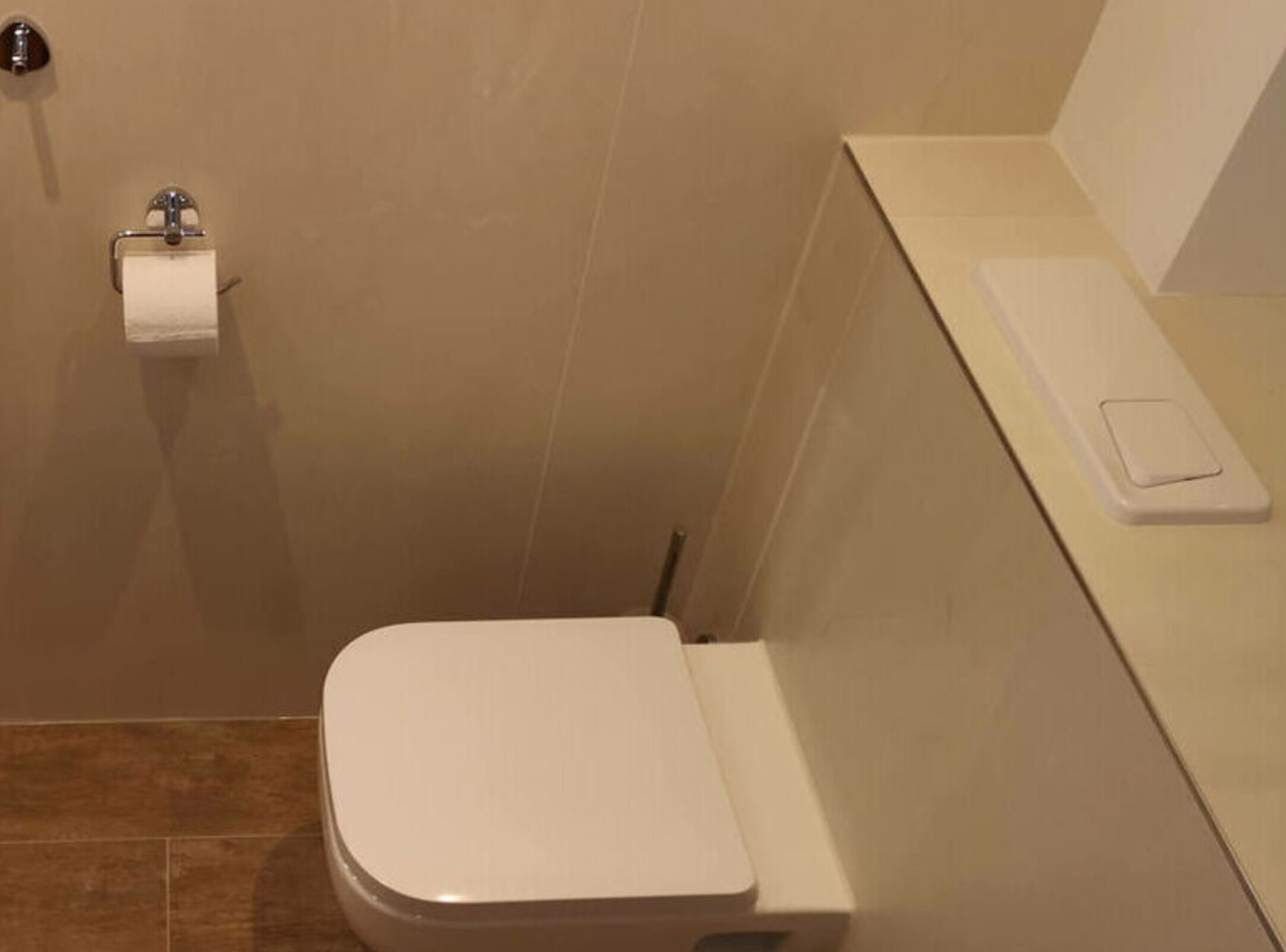 A small, modern bathroom with a white toilet, a paper towel holder, and a soap dispenser on the wall.