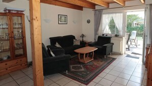A living room with a wooden ceiling, a black sofa, a wooden coffee table, and a glass cabinet with glassware. - Seehund Comfortable Holiday Residence (Otterndorf)