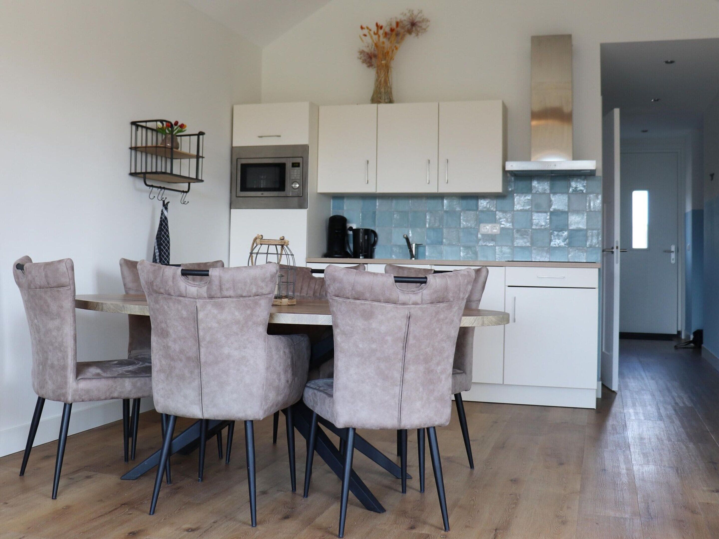 A modern kitchen with white cabinets, a microwave, and a coffee machine. There is a dining table with four chairs.