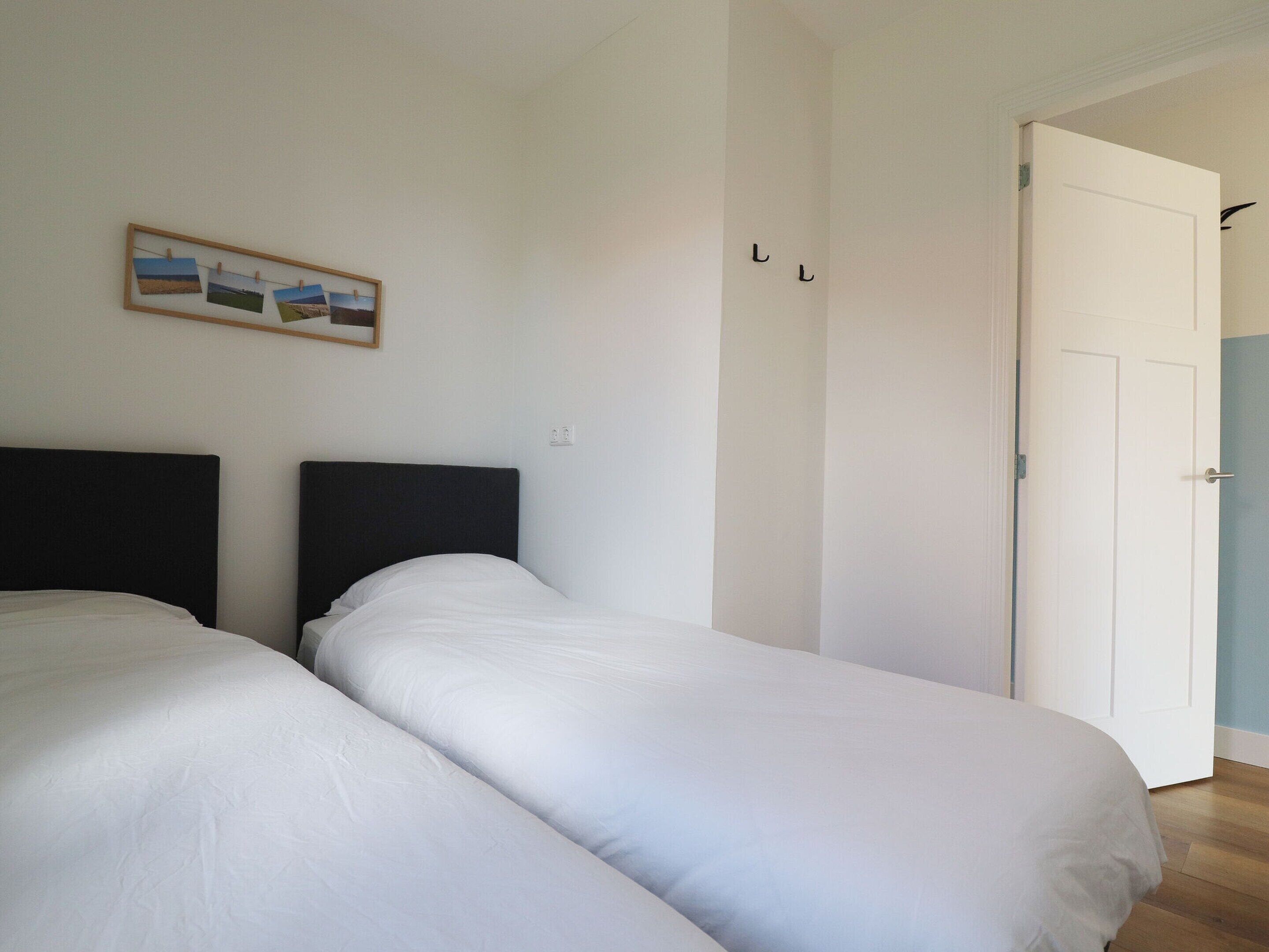 A room with two beds, a door, and a wall-mounted picture.