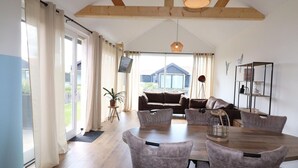 Un comedor amplio con una mesa de madera y sillas tapizadas en gris, un conjunto de sofás y un ventanal con cortinas.