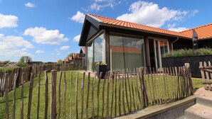 Una casa moderna con techo de tejas rojas, cerca de madera y patio cubierto de césped.