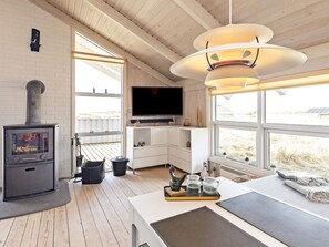 A modern interior with a wood-burning stove, a flat-screen TV, and large windows offering a view of the outdoors. - 4 Star Holiday Home in Hjorring (Hjørring)
