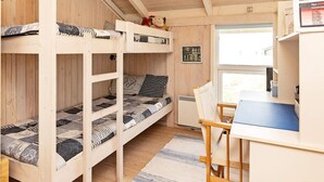 A bunk bed room with a desk and chair, wooden walls, and a window.