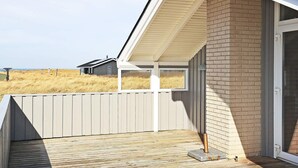 A wooden deck with a metal gate, a brick wall, and a glass door leading to a covered porch.