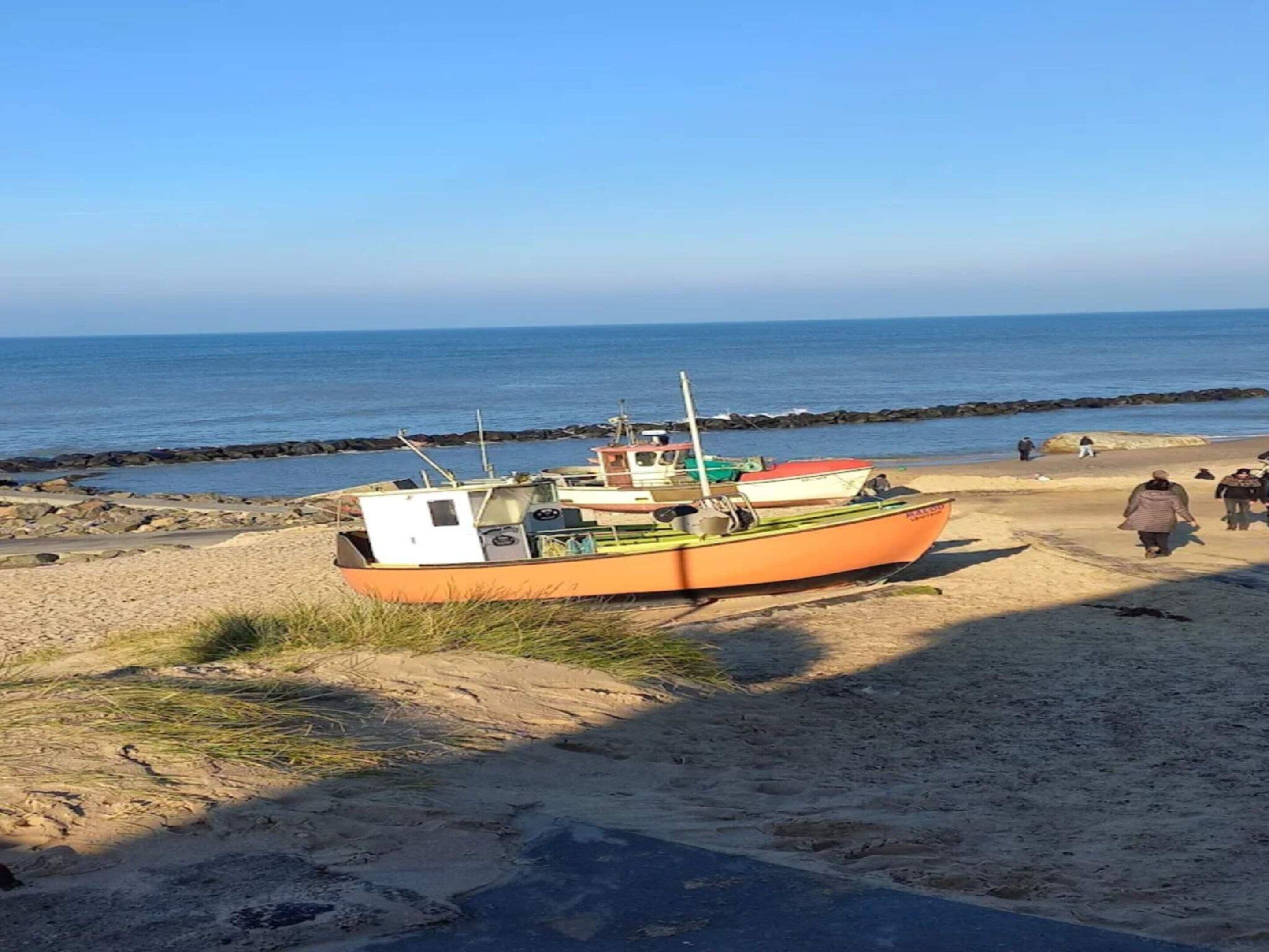 Um barco estacionado numa praia arenosa com um litoral rochoso ao fundo.