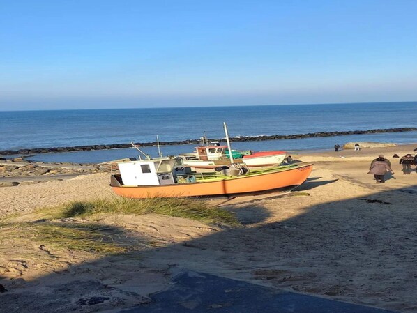 A boat parked on a sandy beach with a rocky shoreline in the background.