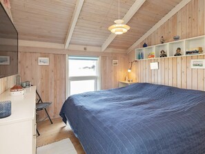 A bedroom with a bed, a desk, a chair, a shelf with decorative items, and a window. - 4 Star Holiday Home in Hjorring (Hjørring)