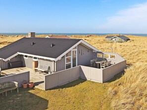 A coastal house with a deck, a dining area, and a view of the sea.