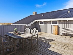 A covered outdoor deck with a table and chairs, a wooden bench, and a building with a dark roof and white siding. - 4 Star Holiday Home in Hjorring (Hjørring)